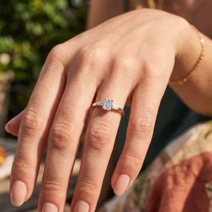 Close-up of a woman's left hand showing a silver ring with an emerald-cut diamond and side baguette stones on the ring finger.