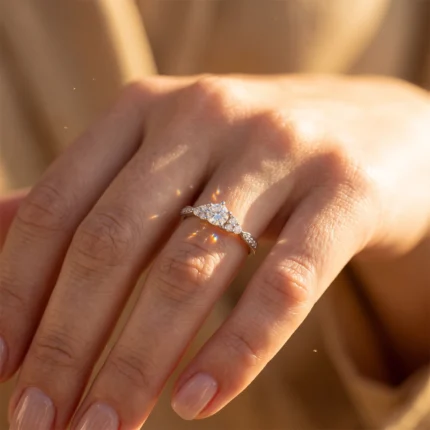 Close-up of a hand wearing a diamond engagement ring with a central round diamond and pavé-set diamonds along the band, in warm sunlight.