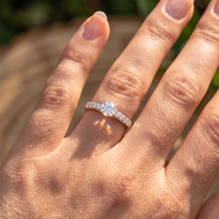 Close-up of a hand wearing a diamond solitaire engagement ring with a pavé band on the ring finger.
