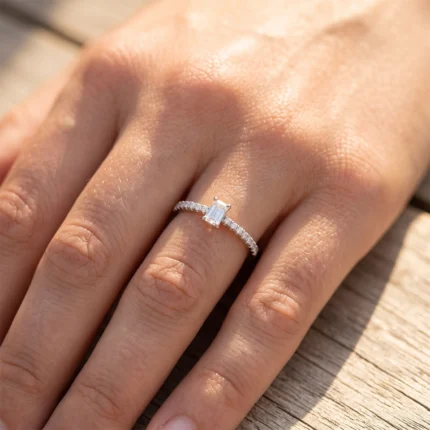 Close-up of a hand wearing an emerald-cut diamond engagement ring with a pavé band on a wooden surface