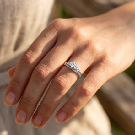 Close-up of a hand wearing a silver engagement ring with a large center diamond and pavé bands on a twisted setting.