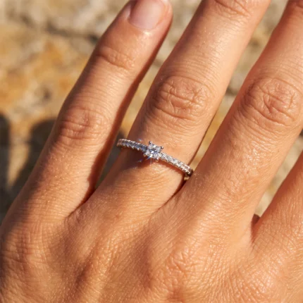 Close-up of a hand wearing a diamond engagement-style ring with a pavé band on the ring finger