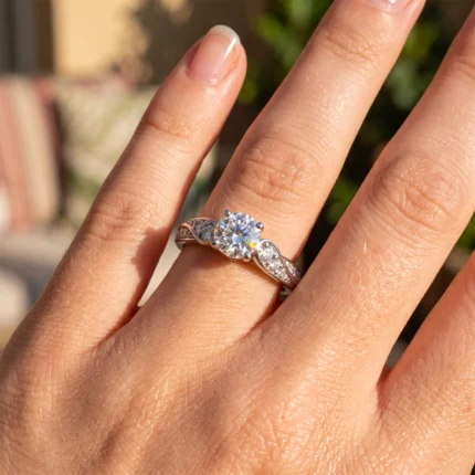 Close-up of a hand with a diamond engagement ring on the ring finger: round center stone with pavé-set side stones on a twisted metal band.