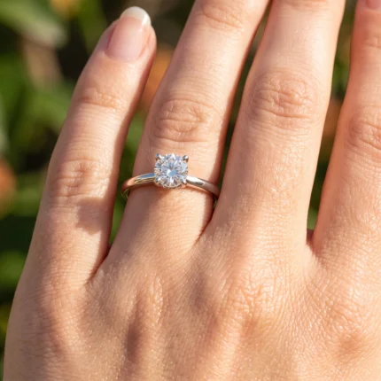 Close-up of a woman's left hand wearing a silver engagement ring with a round-cut diamond.