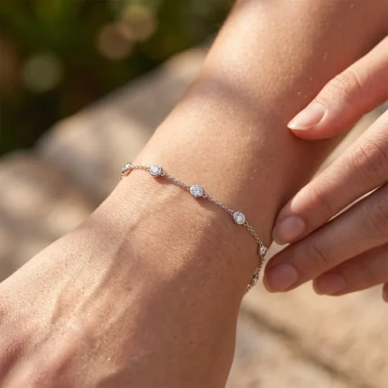 Close-up of a woman's wrist wearing a silver bracelet with small diamond-studded circles in sunlight, outdoors.