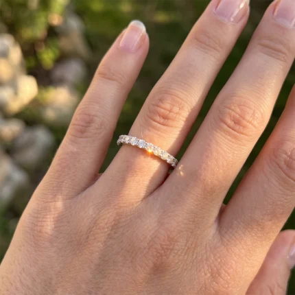 Close-up of a hand wearing a diamond eternity ring on the ring finger, outdoors in warm sunlight.