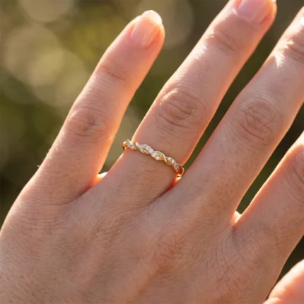 Close-up of a gold ring with diamond-accent twist on the finger, warm sunlight on the skin.