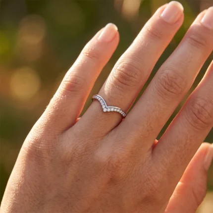 Close-up of a hand wearing a silver heart-shaped diamond ring on the ring finger in warm sunlight.