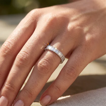 Close-up of a hand wearing a silver ring with a row of baguette-cut diamonds, sunlight catching the stones.