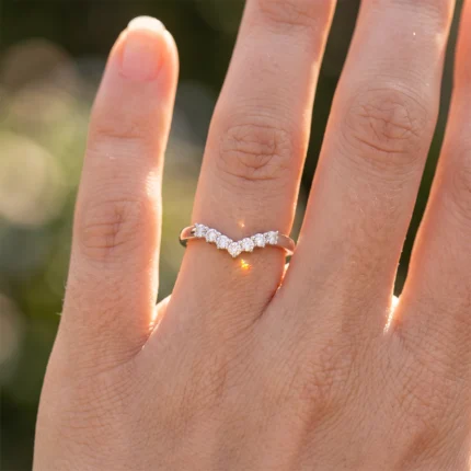 Close-up of a hand showing a diamond V-shaped ring on the ring finger in sunlight.