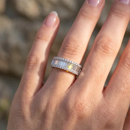 Close-up of a hand wearing a two-row diamond ring with baguette-cut stones and small pavé accents in silver metal.