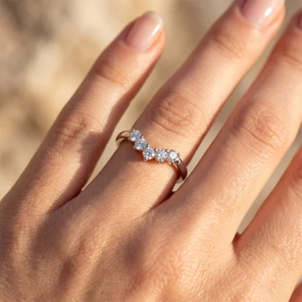 Close-up of a hand wearing a thin gold ring set with alternating small diamonds along the band on a sunny backdrop