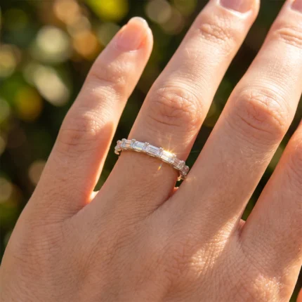 Close-up of a hand wearing a silver diamond-studded ring on the ring finger, with a blurred green background.
