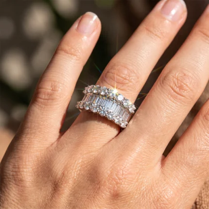 Close-up of a hand showing three silver diamond-studded rings on the ring finger, catching sunlight.