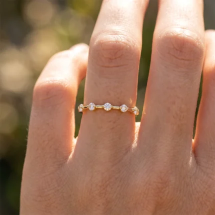 Delicate gold ring with alternating round diamonds on a finger in sunlight.