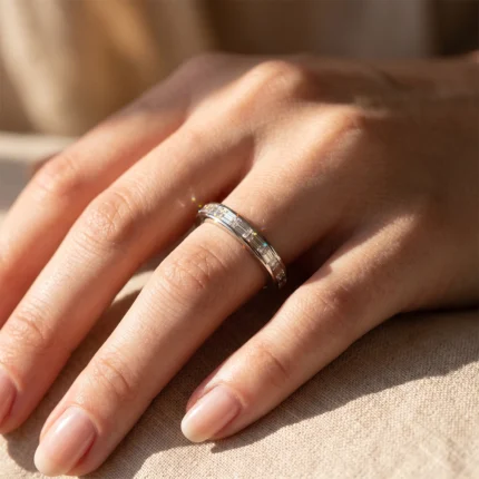 Close-up of a hand wearing a silver ring with diamonds on the ring finger, in warm light.