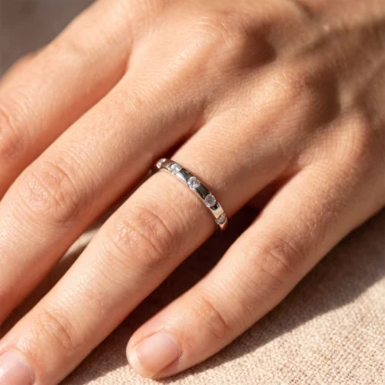 Close-up of a silver band ring with small diamonds worn on a finger.