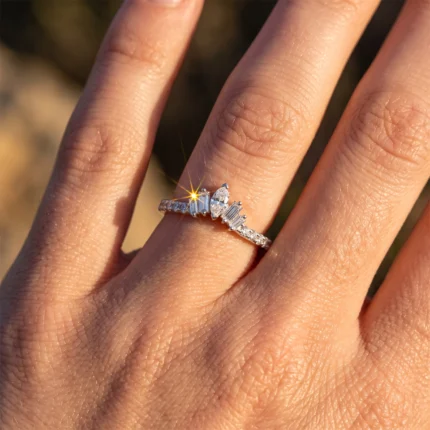 Close-up of a diamond ring on the ring finger, sunlight creating a bright sparkle on the central stone and side diamonds.