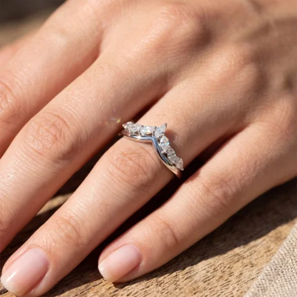 Close-up of a finger wearing a curved silver ring with multiple diamonds along the band