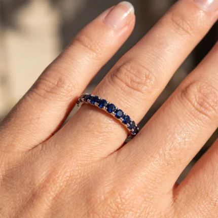 Close-up of a hand wearing a thin silver ring set with blue sapphires along the band on the finger.