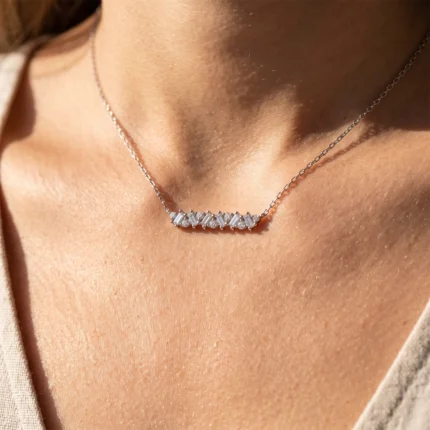 Close-up of a silver necklace with a row of baguette-cut diamonds resting on a woman's collarbone area.