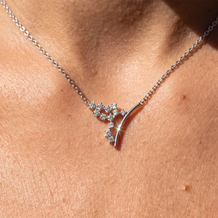Silver chain necklace with a diamond-encrusted twig/branch pendant resting on skin, sparkling in sunlight.