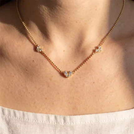Gold necklace with small heart-shaped diamond clusters resting on the collarbone.