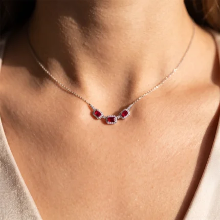 Silver necklace with red square-cut gems outlined by small diamonds on a woman's neck.