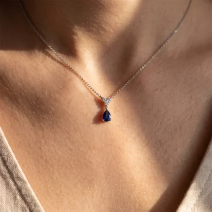 Silver chain necklace with a teardrop blue gemstone pendant resting on the collarbone.