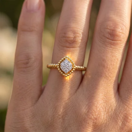 Gold ring with a square cluster of diamonds on a beaded band worn on a finger.
