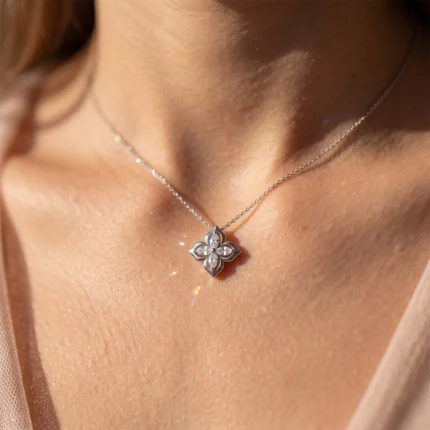 Silver necklace with a four-petal flower pendant encrusted with small diamonds resting on the neck décolletage.