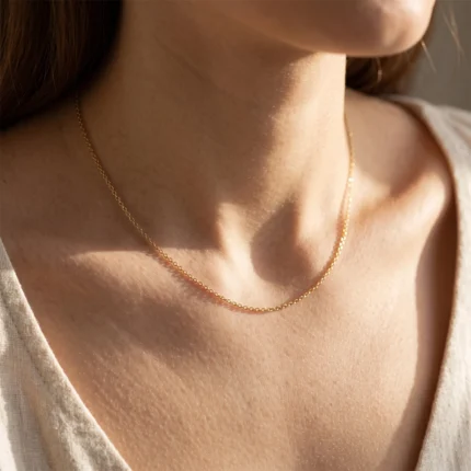 Close-up of a woman's neck with a thin gold chain resting on the collarbone in soft sunlight.