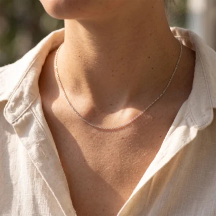 Close-up of a neck with a lightweight silver chain necklace over a beige linen shirt.
