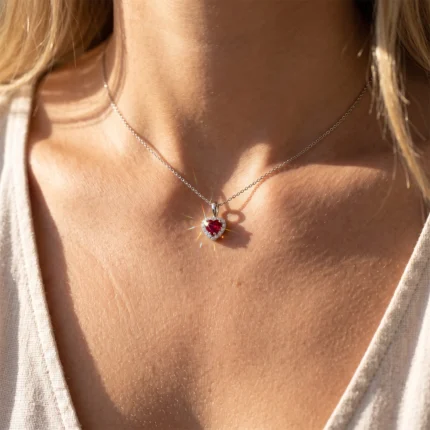 Silver heart pendant with a red gemstone on a delicate silver chain resting on the collarbone.