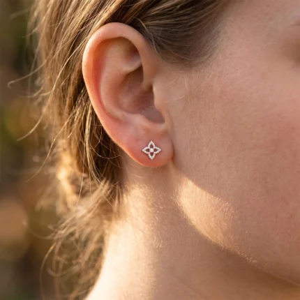 Close-up of a woman's ear with a silver diamond-studded four-point flower earring on the earlobe.