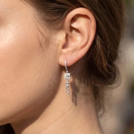 Close-up of a woman's ear wearing a diamond-studded drop earring with a square pendant and dangling strands.