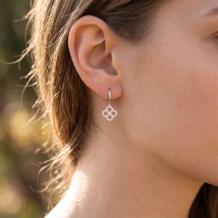 Close-up of a woman's ear wearing a silver hoop earring with a diamond-studded four-leaf clover pendant.