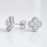 Flower-shaped diamond stud earrings in white gold/silver with a central cluster and pavé-set stones, displayed on a reflective surface, brand name Ditani on the post.
