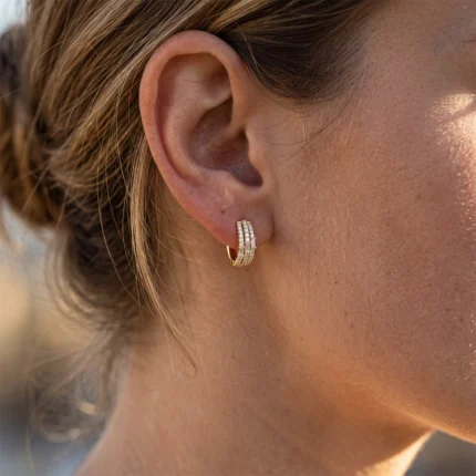 Close-up of a woman's ear wearing a gold diamond-studded hoop earring.