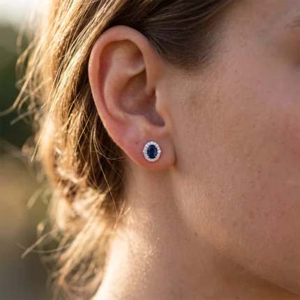 Close-up of a ear with a blue oval sapphire stud surrounded by small diamonds
