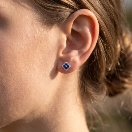 Close-up of a woman's ear with a blue flower-shaped stud earring surrounded by small white stones.