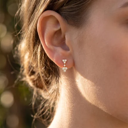 Close-up of a woman's ear with a gold-tone diamond drop earring featuring three tiny floral clusters hanging along the lobe.