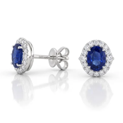 Oval blue sapphire stud earrings surrounded by a halo of diamonds set in white metal (likely white gold).