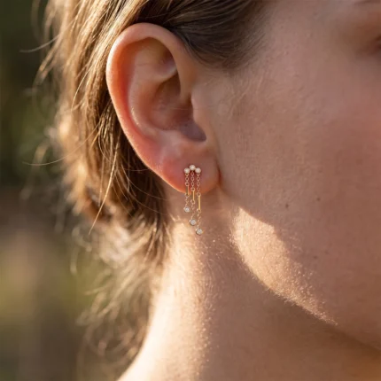 Close-up of a pierced ear wearing a delicate gold dangle earring with small diamond-like stones and hanging chains.