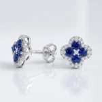 Silver stud earrings featuring blue sapphire flowers surrounded by diamonds on a white background, with butterfly-style backing visible.