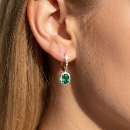 Close-up of an earlobe with a diamond-studded hoop earring featuring a green emerald pendant.