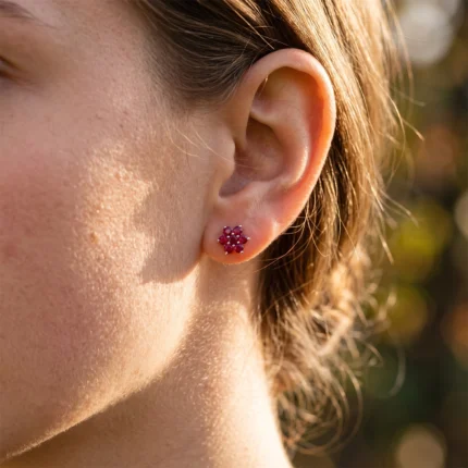 Close-up of a person's ear with a red flower-shaped ruby stud earring on the earlobe.