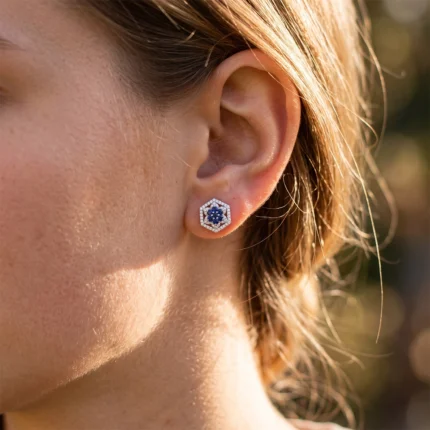 Hexagonal stud earring with a blue center gemstone and surrounding clear stones on an ear.