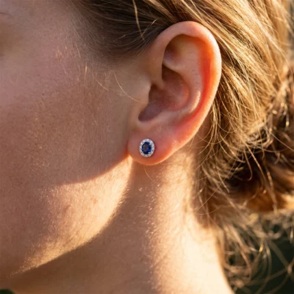 Close-up of an ear with a blue sapphire halo stud earring surrounded by small diamonds.