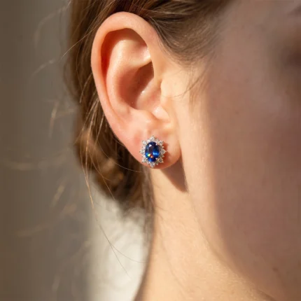 Close-up of an ear wearing a blue sapphire stud with a surrounding diamond halo on the earlobe.